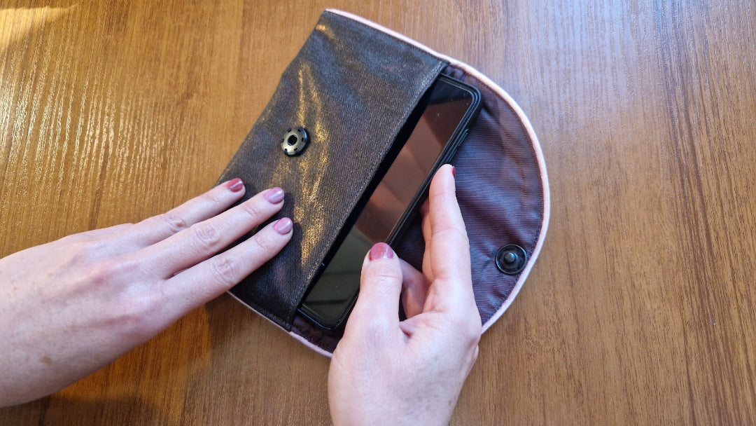 Hands putting a mobile phone in a purse with EMF protection
